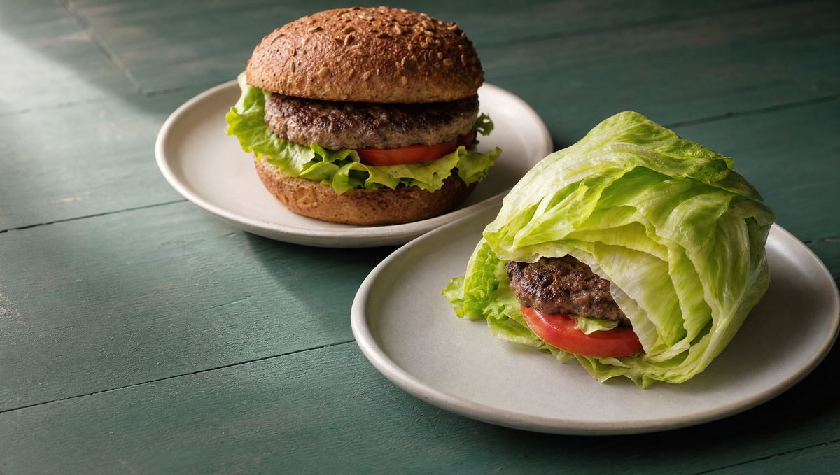 Burger on barley bread and a lettuce-wrapped burger on a green table